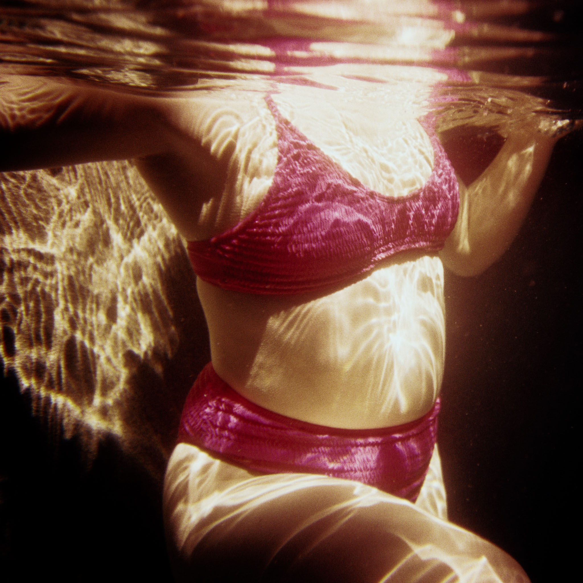 Swimmer in a red swimsuit in black water at night, lit by a single flash — 35mm cross-processed Fuji Velvia, Port Douglas